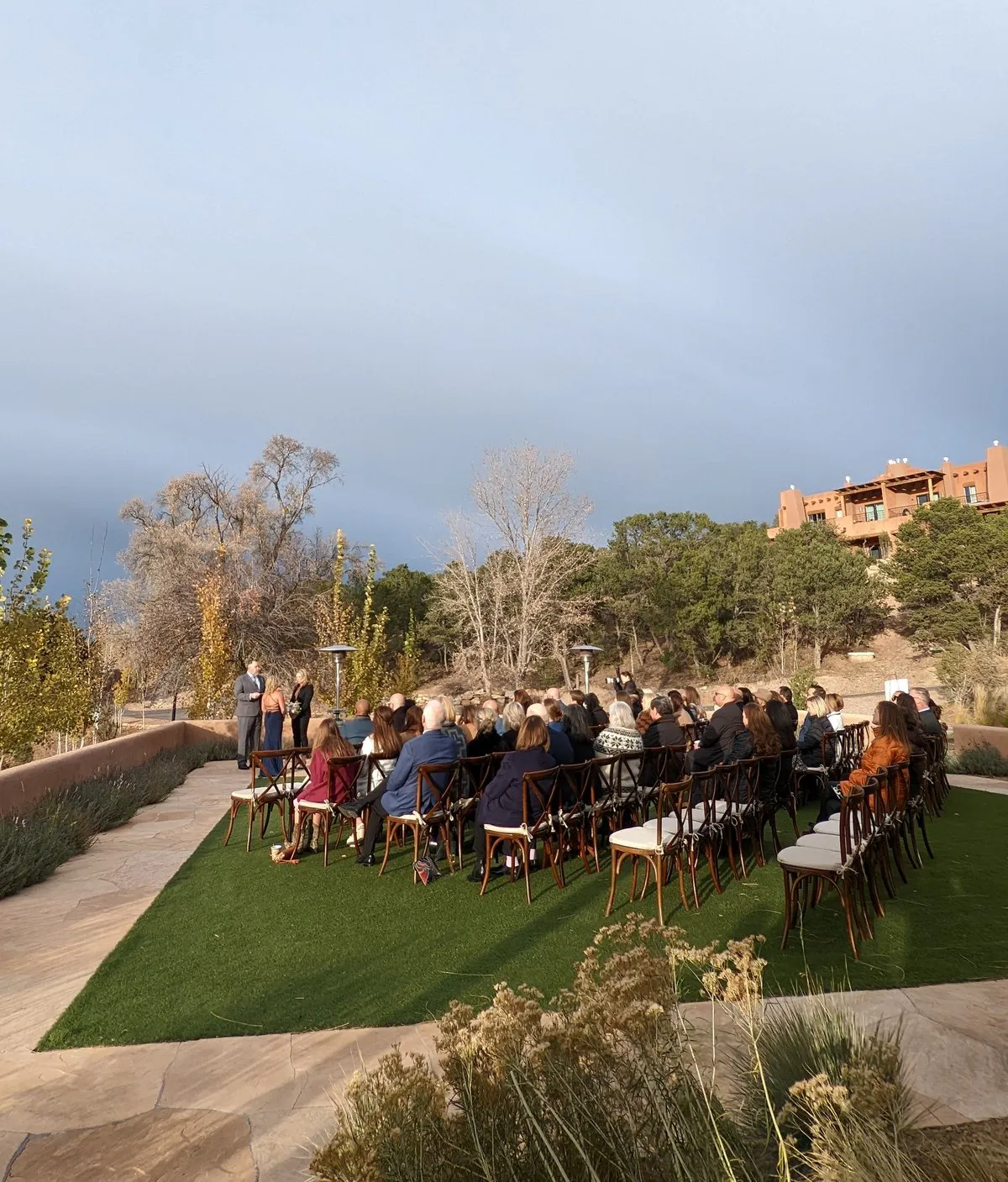 An outdoor wedding ceremony on a lawn at Bishop's Lodge, with Santa Fe mountains and adobe architecture in the background