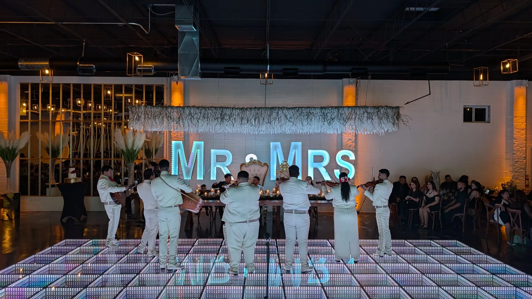 A mariachi band performing at a wedding reception inside D'Venue, in front of a lit-up MR & MRS marquee sign