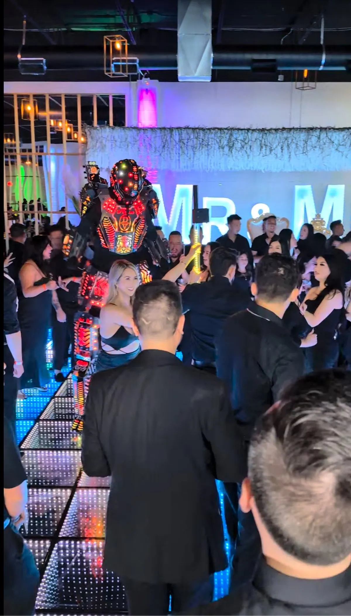 A guest interacting with an LED robot performer on the lit dance floor at D'Venue