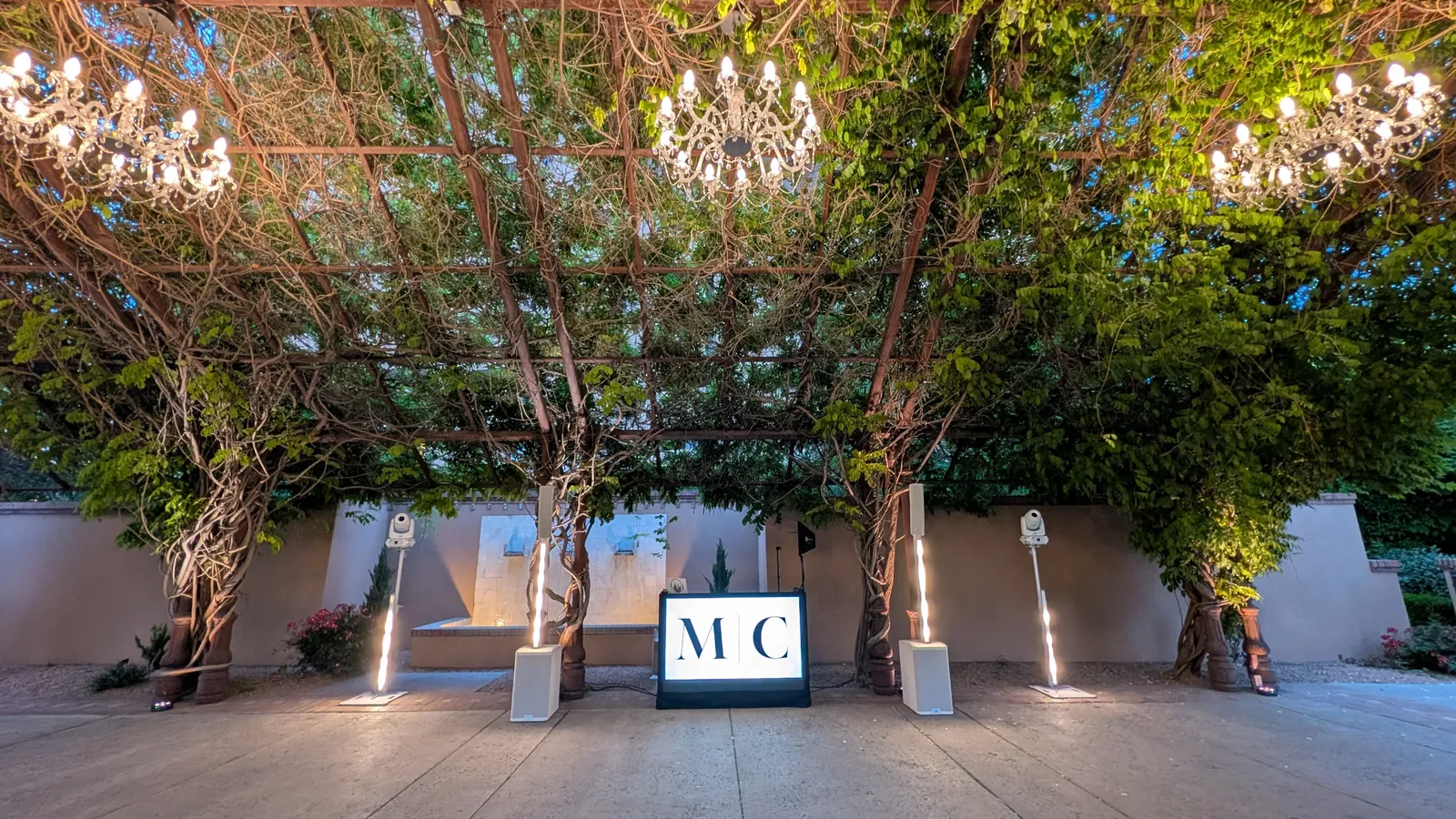 An En Blanc setup with a monogrammed booth under a string-lit garden trellis