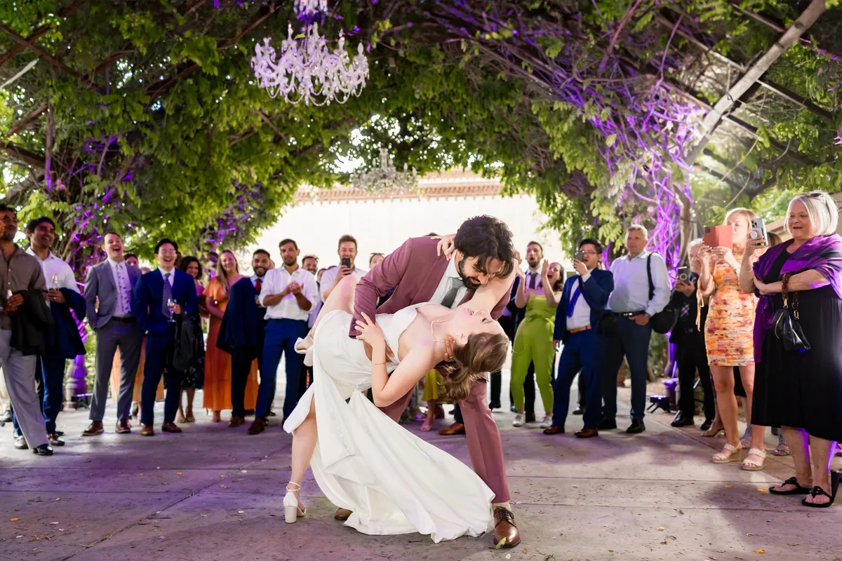 A couple dipping and kissing under a wisteria arbor