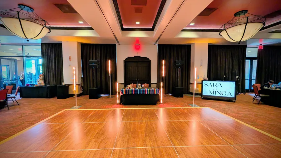 The dance floor and DJ booth set up for a reception at The Event Center at Sandia Golf Club, with uplit totem columns and a red-lit backdrop