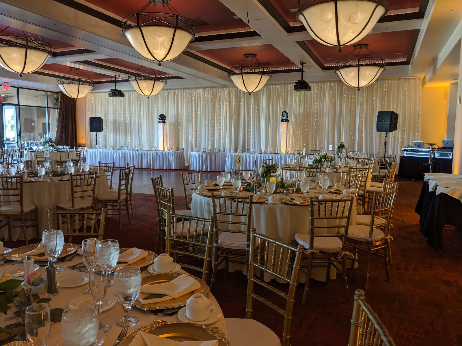 A Cutmaster Music reception setup at The Event Center at Sandia Golf Club, with round tables, a fairy-light backdrop, and mirrored uplit columns flanking the head table