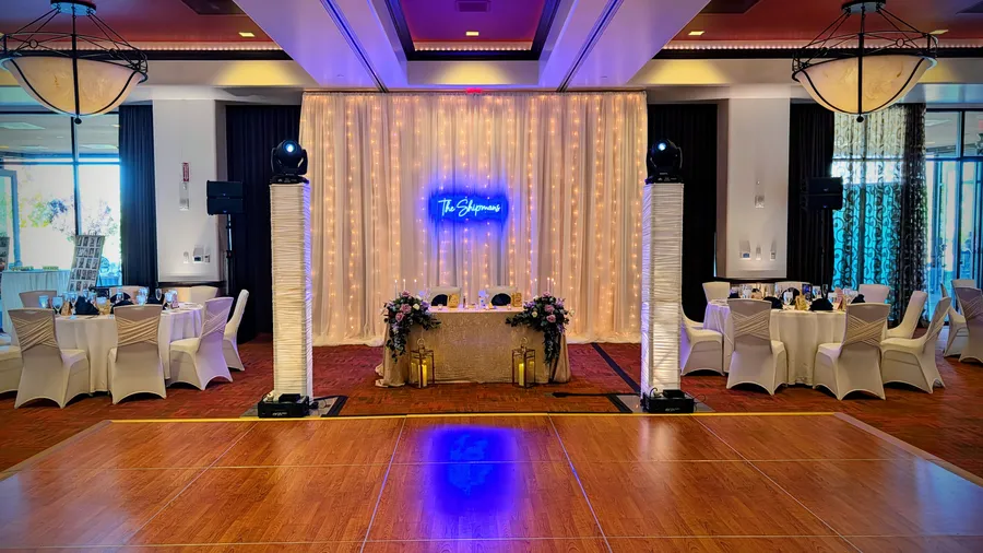 A sweetheart table at The Event Center at Sandia Golf Club, framed by a fairy-light curtain backdrop and uplit totem columns with moving-head lights