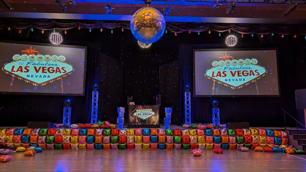 A Las Vegas-themed corporate party stage in the Sandia Ballroom, with a disco ball and colorful balloon wall