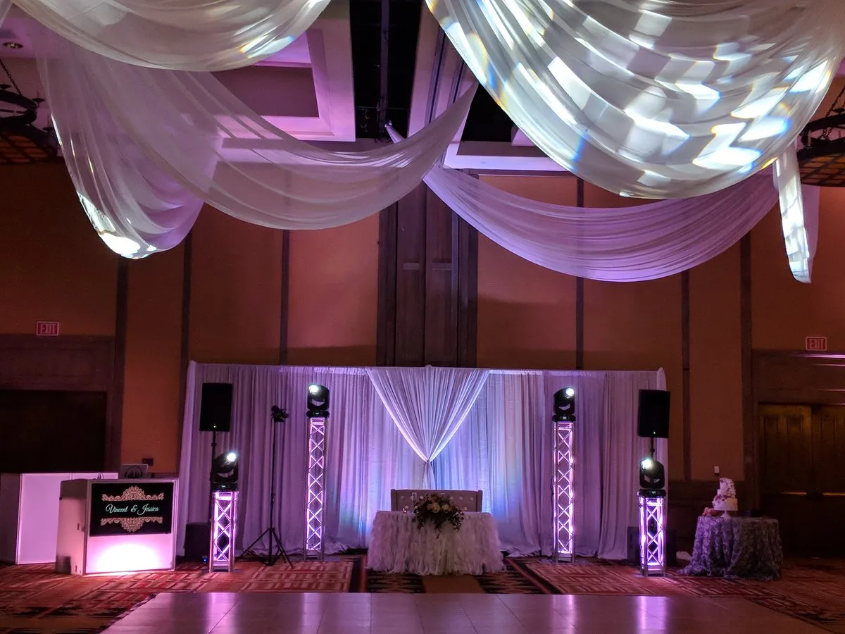 A Cutmaster Music DJ booth and sweetheart table backdrop set up in the Tamaya Ballroom, lit in purple